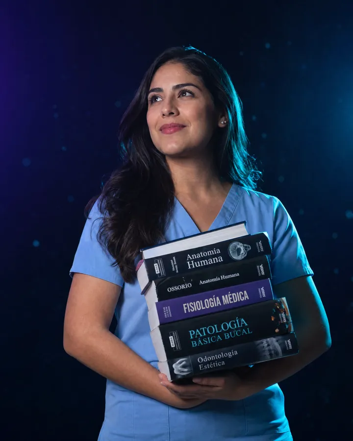 Odontóloga con uniforme sanitario sosteniendo libros de Anatomía Humana, Fisiología Médica y Patología Bucal para preparar la homologación